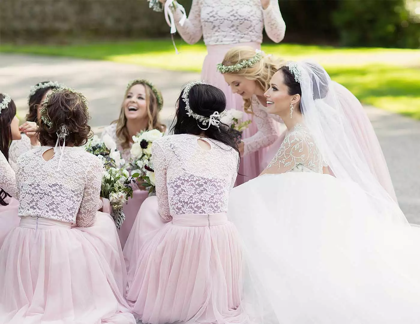 Destination wedding in Ireland — bride surrounded by her bridesmaids, kneeling together and smiling during a wedding celebration.