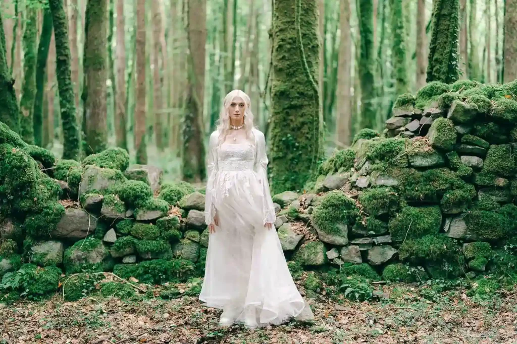 Destination wedding at Ashford Castle, County Mayo — bridal portrait in a mossy forest, with the bride looking directly at the camera in a white wedding gown.