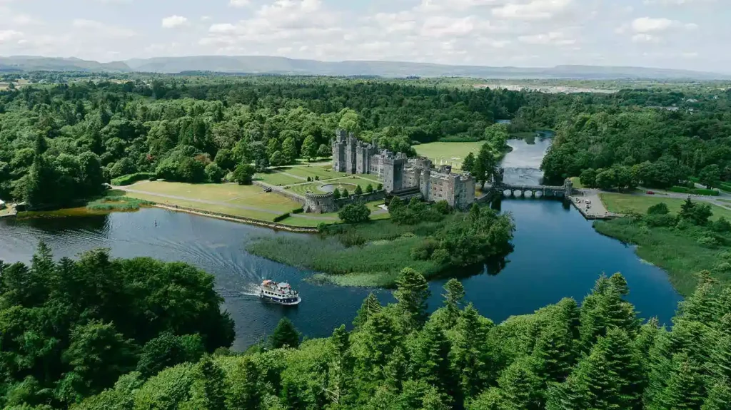 Destination wedding at Ashford Castle, County Mayo — aerial drone view of the estate showing the castle, surrounding forest, and nearby lake within the wider grounds.