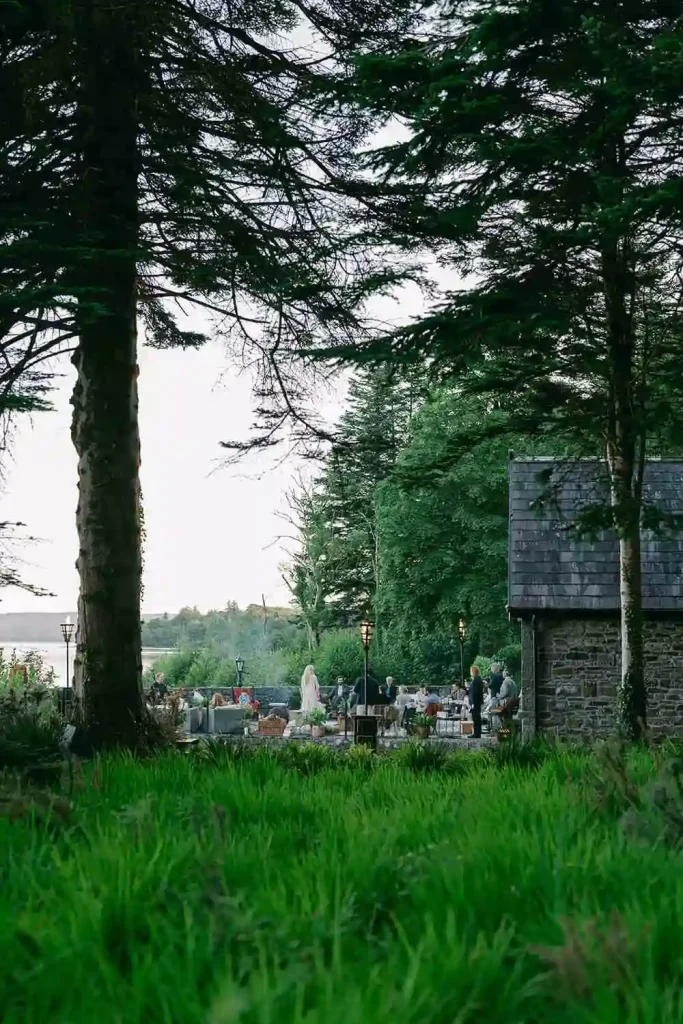 Destination wedding ceremony at Ashford Castle, County Mayo — summer solstice party on a lakeside dock with guests gathered on lounge seating, enjoying live entertainment beside the water.