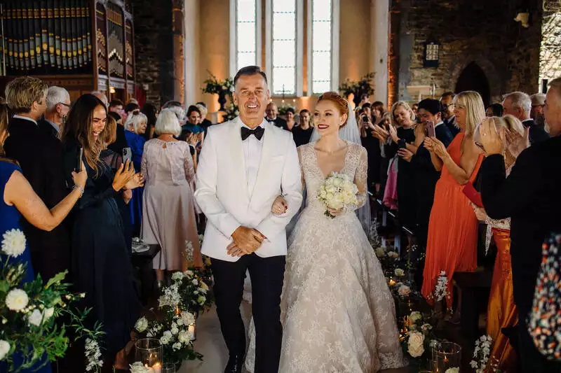 Destination wedding ceremony at Ballynahinch Castle, County Galway, Ireland — bride and groom walking back down the aisle linked arm in arm, smiling as guests line both sides of the aisle reacting and celebrating the ceremony exit.