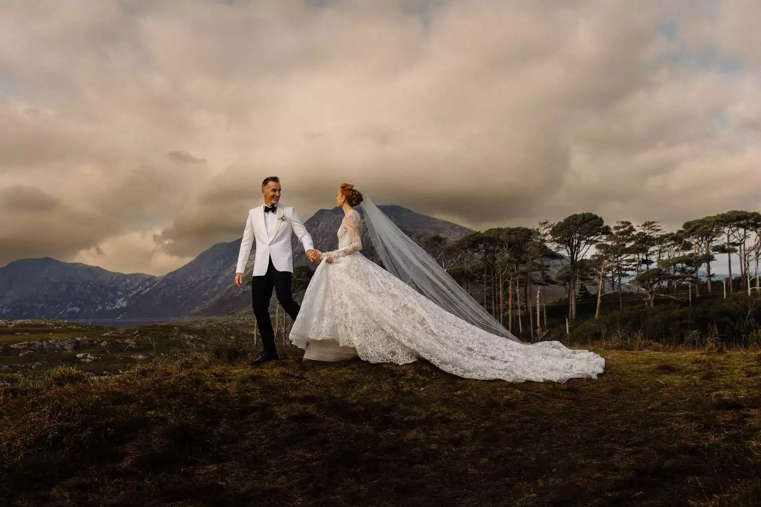 Destination wedding at Ballynahinch Castle, County Galway — bride and groom walking hand in hand through the Connemara landscape while looking at one another.