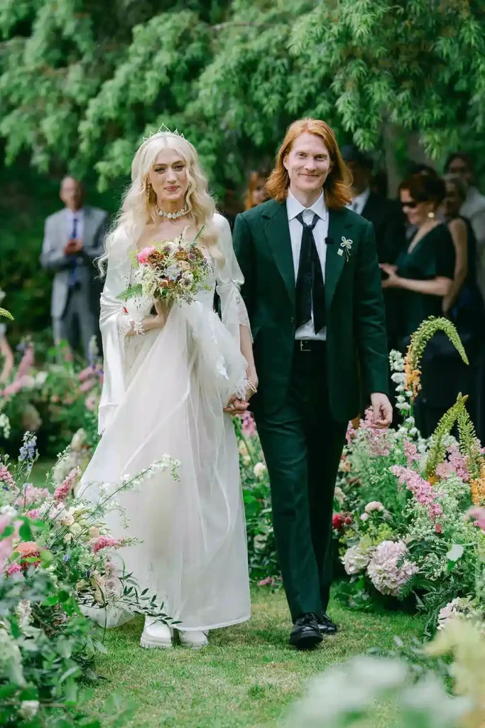 Destination wedding ceremony at Ashford Castle, County Mayo — bride and groom smiling during an outdoor wedding recessional, holding hands as the bride carries a colourful wedding bouquet.