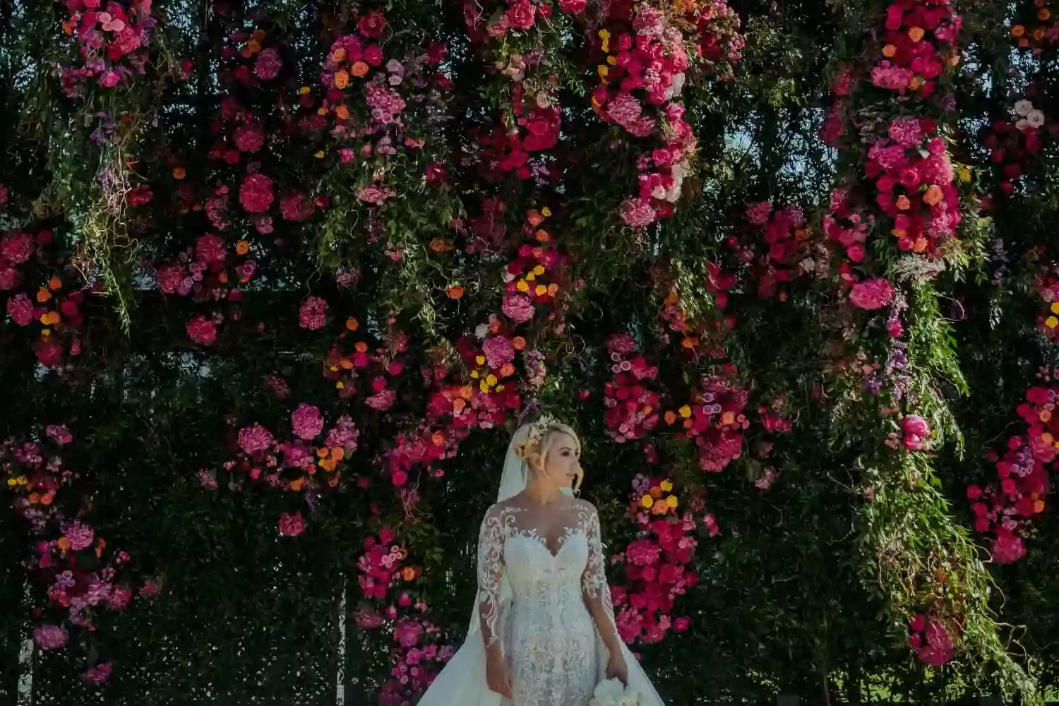 Destination wedding in Ireland — bride standing before a large floral installation with seasonal blooms creating a decorative backdrop.