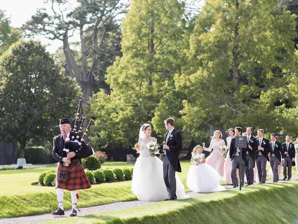 Irish castle wedding at Ashford Castle, County Mayo — bride and groom escorted to the castle by a traditional Irish bagpiper following the ceremony.