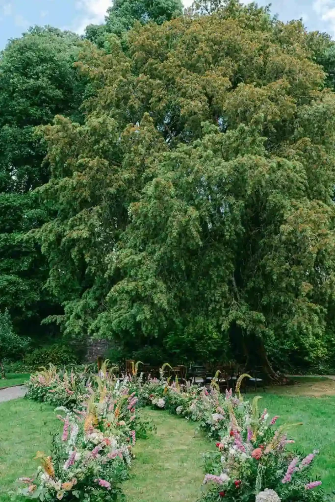 Irish destination wedding at Ashford Castle, County Mayo — curved floral aisle leading to an outdoor ceremony altar beneath a large tree on the estate grounds.