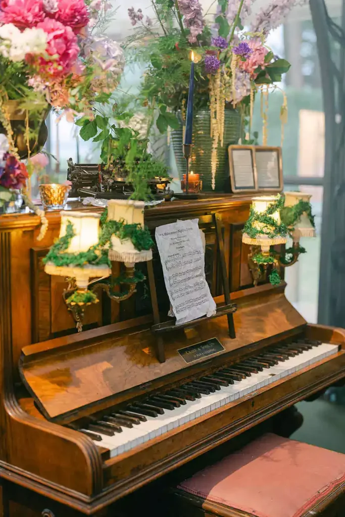 Upright wooden piano decorated with vibrant flower arrangements, candles, greenery, and a sheet of music on the stand.