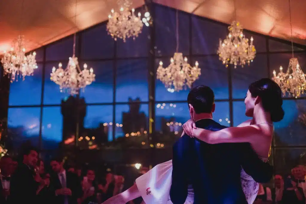 Destination wedding in Ireland — bride carried by the groom beneath chandeliers during a late-night celebration at an Irish castle wedding venue, with guests gathered ahead.