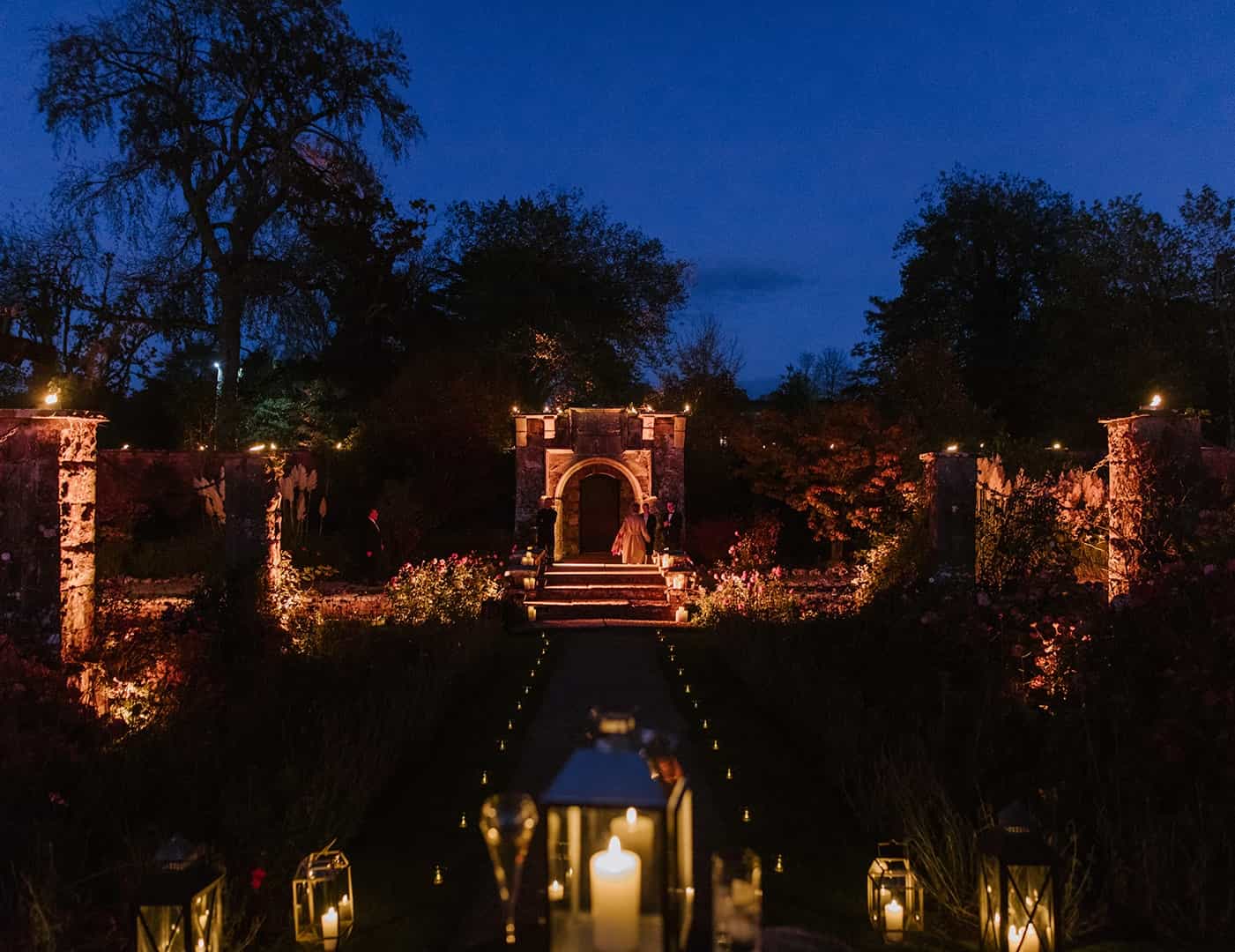 Destination wedding in Ireland — stone archway at an Irish wedding venue with candlelit pathways and guests gathered outdoors during an evening celebration.