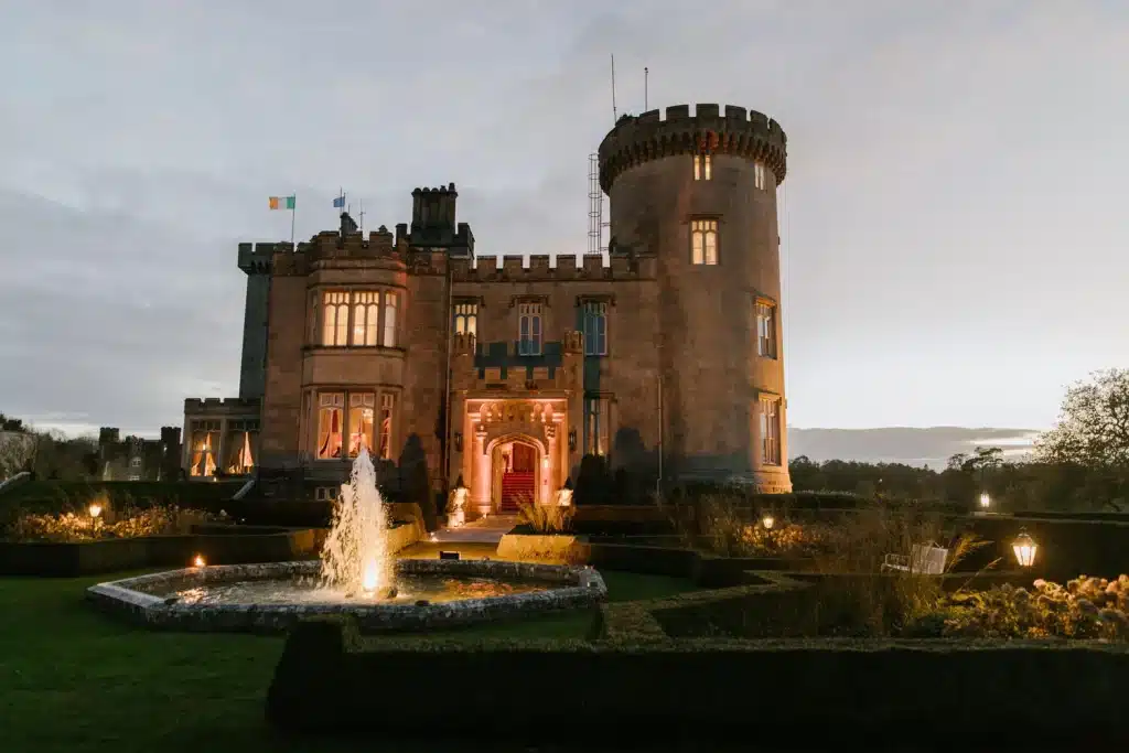 Castle weddings Ireland at Dromoland Castle, County Clare — original castle exterior illuminated at dusk beside the estate fountain and gardens.
