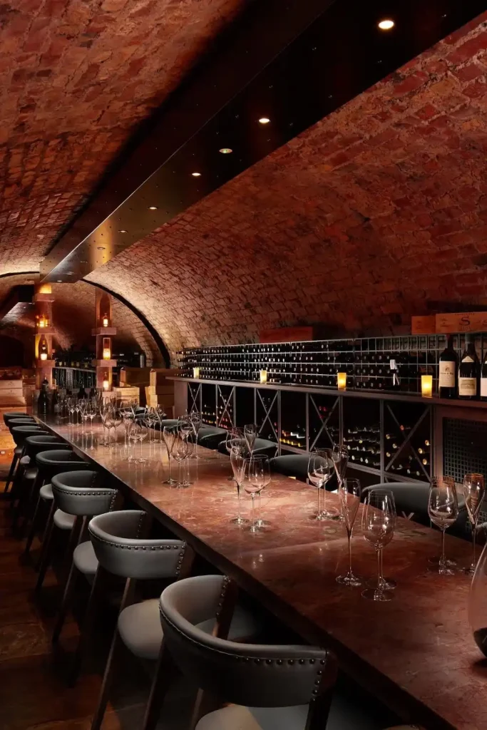 Luxury events Ireland at Adare Manor, County Limerick — The Cellar wine room prepared for a tasting experience with a long table set with wine glasses, warm candlelight, and rows of wine storage visible in the background within the atmospheric stone interior.
