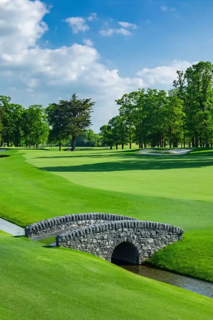 Irish castle wedding at Adare Manor, County Limerick — manicured golf course landscape with lush green fairways, a small stone bridge crossing water, and mature trees set against an open blue sky within the estate grounds.
