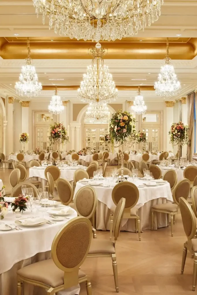 Destination wedding at Adare Manor, County Limerick — The Grand Ballroom set for a wedding reception featuring warm ambient lighting, ornate chandeliers, round dining tables, and tall floral arrangements with candles arranged across the ballroom floor.