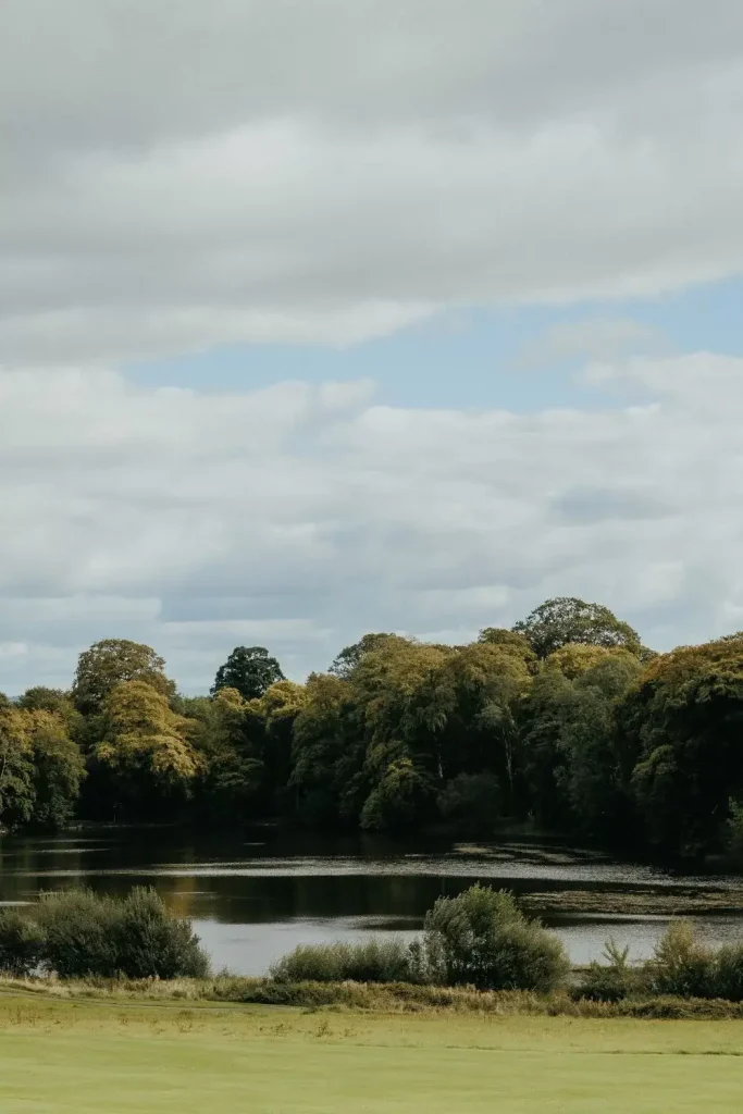 Destination wedding in Ireland Ballyfin Demesne, County Laois — tranquil estate lake framed by mature woodland and full tree canopies, with still reflective water set within the historic wedding grounds.