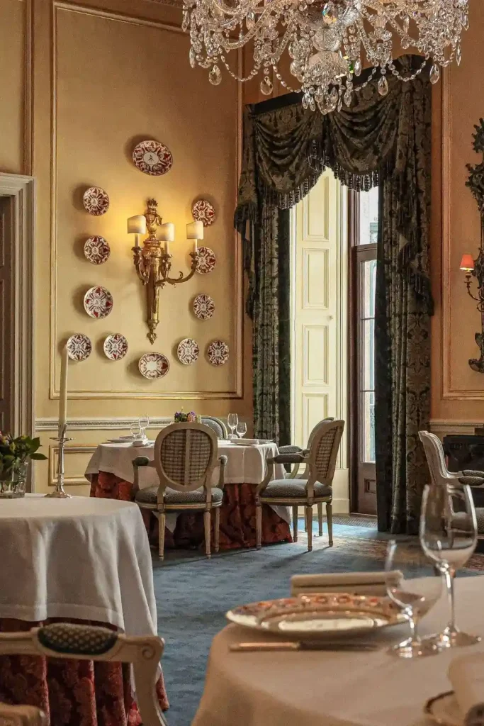 Irish destination wedding at Ballyfin Demesne, County Laois — State Dining Room arranged with round banquet tables, fine dining place settings, and upholstered chairs within an elegant interior prepared for a formal evening reception.