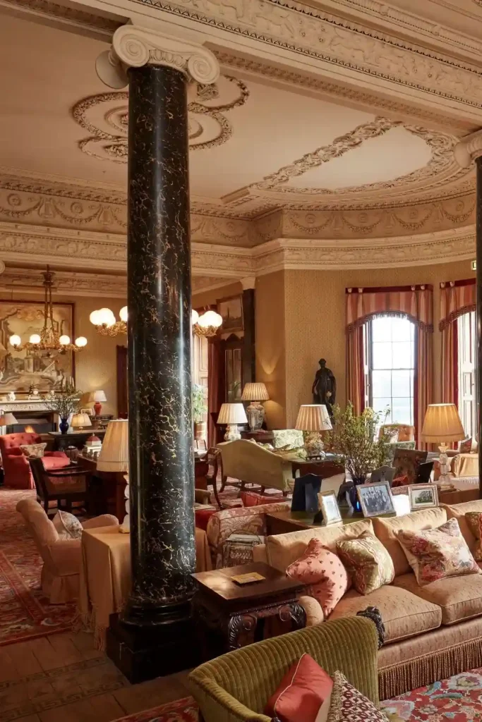 Destination wedding in Ireland Ballyfin Demesne, County Laois — The Library with lounge seating, ornate ceiling detailing, framed paintings, gold accents, and hanging lamps within an elegant heritage interior.