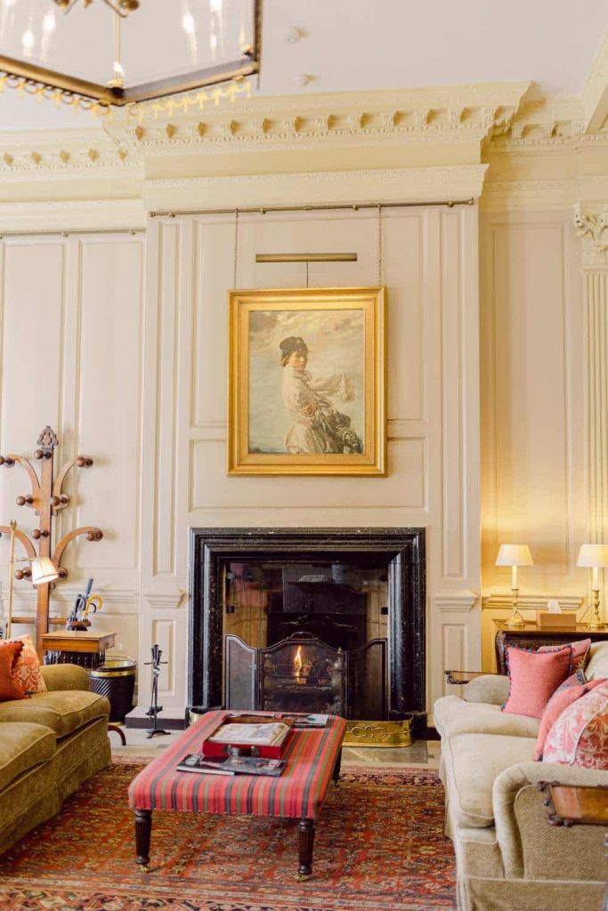 Irish destination wedding at Cashel Palace, County Tipperary — elegant foyer lounge with a central fireplace and a portrait painting above the mantel, set within a heritage estate interior featuring soft seating and classical architectural detailing.