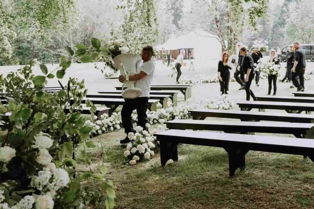 Destination wedding ceremony setup at Lough Eske Castle, County Donegal — floral-lined aisle being assembled on the estate grounds, with event staff positioning large urn arrangements and refining garden-style ceremony details in preparation for an outdoor wedding.