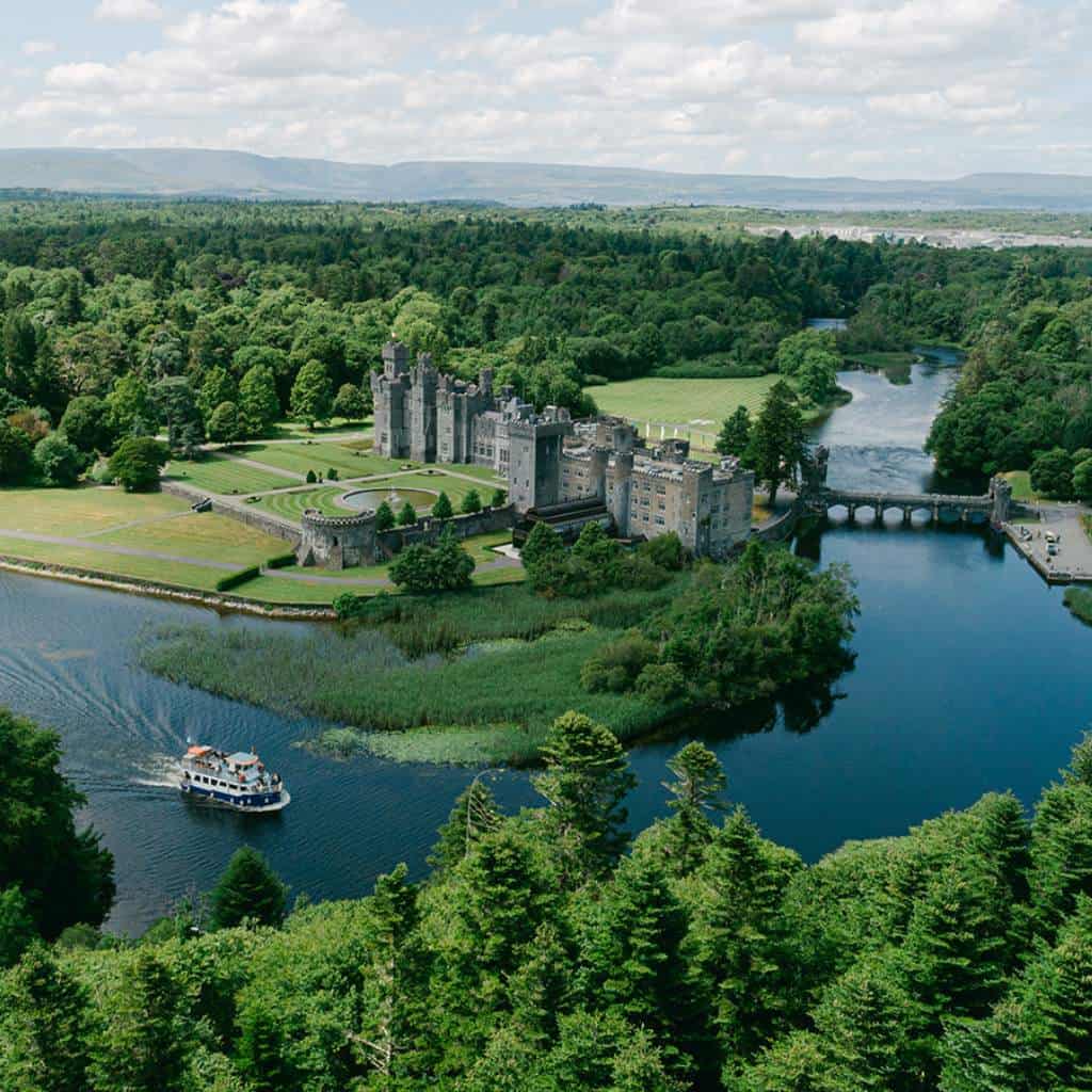 Irish castle wedding in Ireland — Ashford Castle aerial drone view on a bright day with Lough Corrib below and a boat crossing the lake beside the estate.