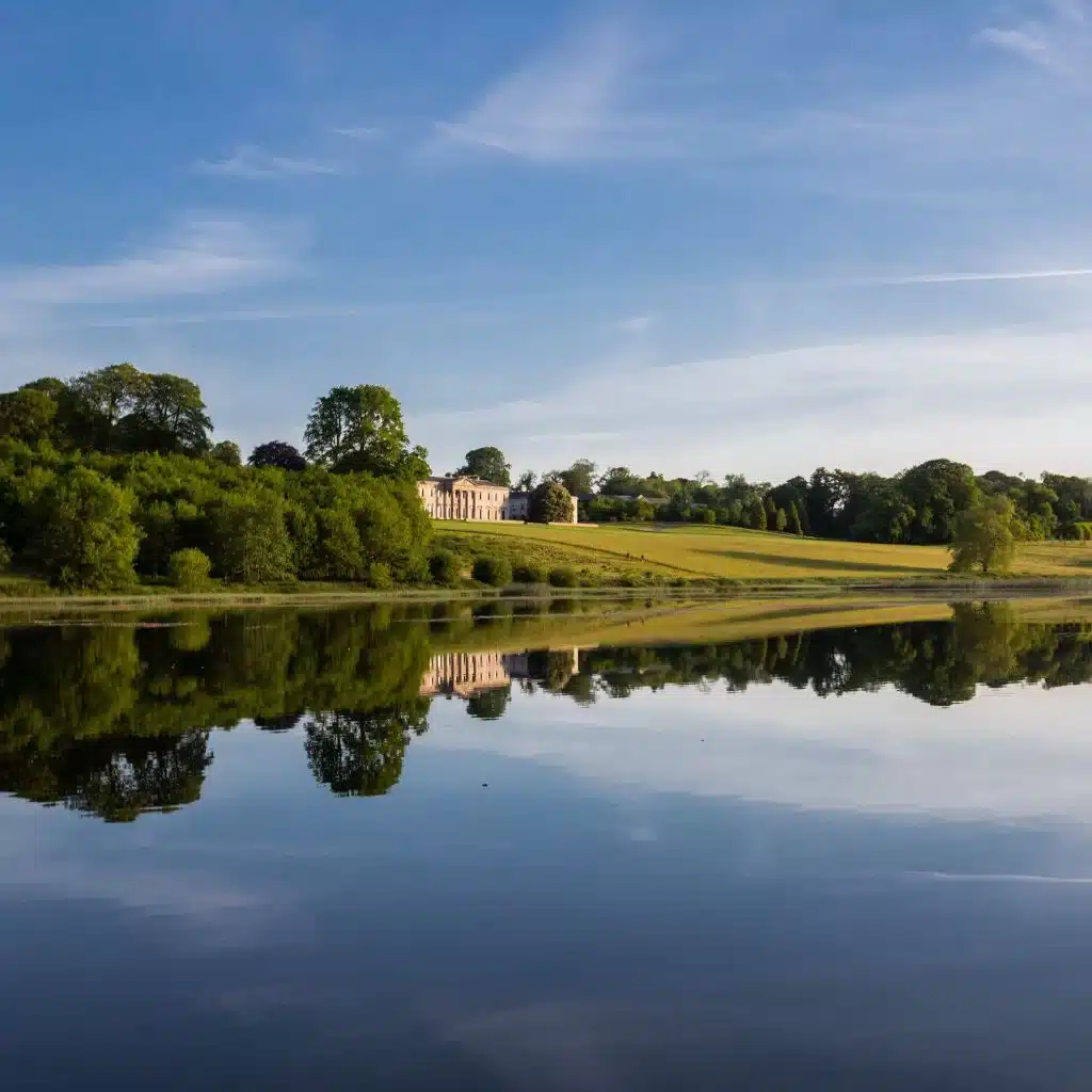 Irish destination wedding Ballyfin Demesne, County Laois, Ireland — exterior view of the estate overlooking a lake, framed by mature trees with the main property visible in the distance across the grounds.