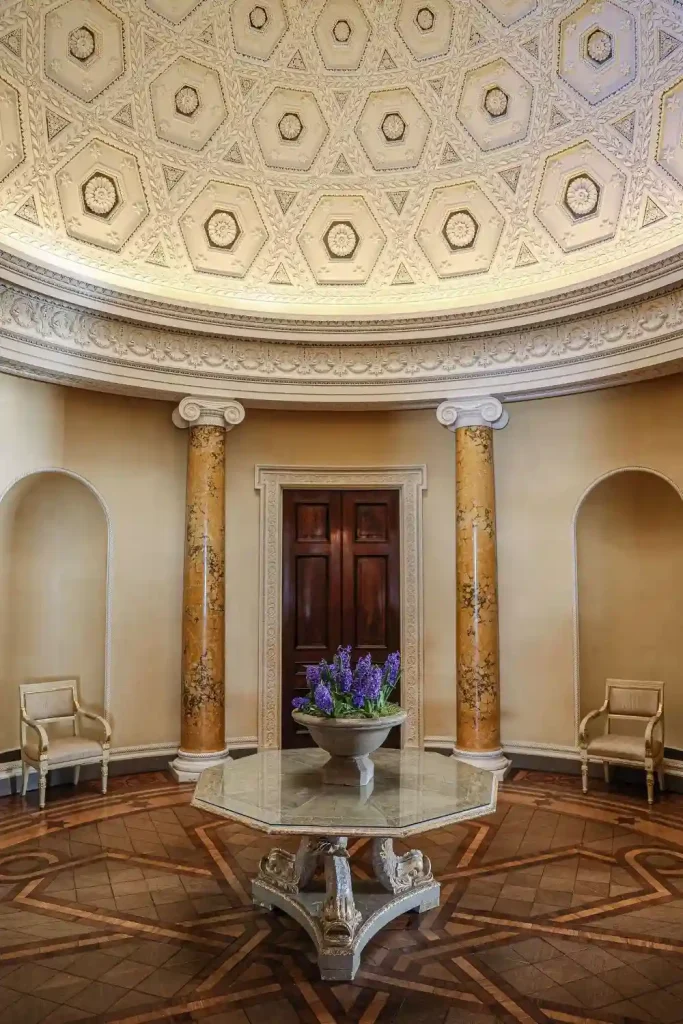 Irish destination wedding Ballyfin Demesne, County Laois, Ireland — the Rotunda featuring a circular corridor with a high ceiling and intricate detailing, with paired pillars either side of a doorway and a central table styled with a floral arrangement.