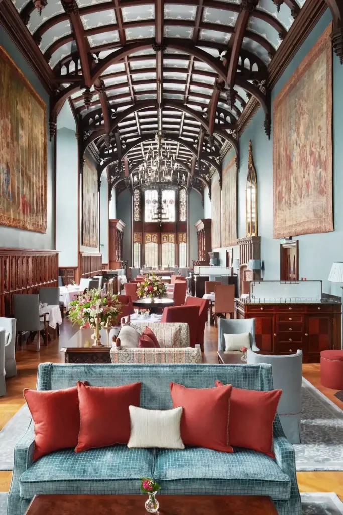 Luxurious hotel lounge with blue sofa, red cushions, and a grand arched wooden ceiling in a long ornate hall.