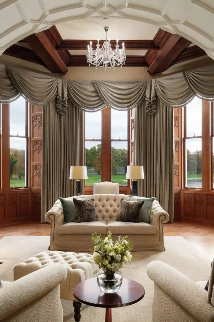 Irish castle wedding at Adare Manor, County Limerick — Lady Caroline Suite featuring light upholstered seating, a fresh vase of flowers, and large windows with soft draping that fills the suite with natural light within the castle setting.