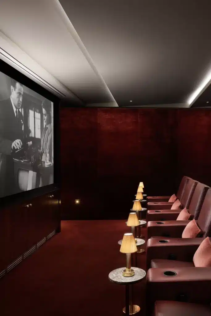 Irish castle wedding at Adare Manor, County Limerick — private cinema screening room with rows of red cushioned seats, low ambient lighting from side table lamps, and a black and white film playing across the cinema screen within the castle interior.