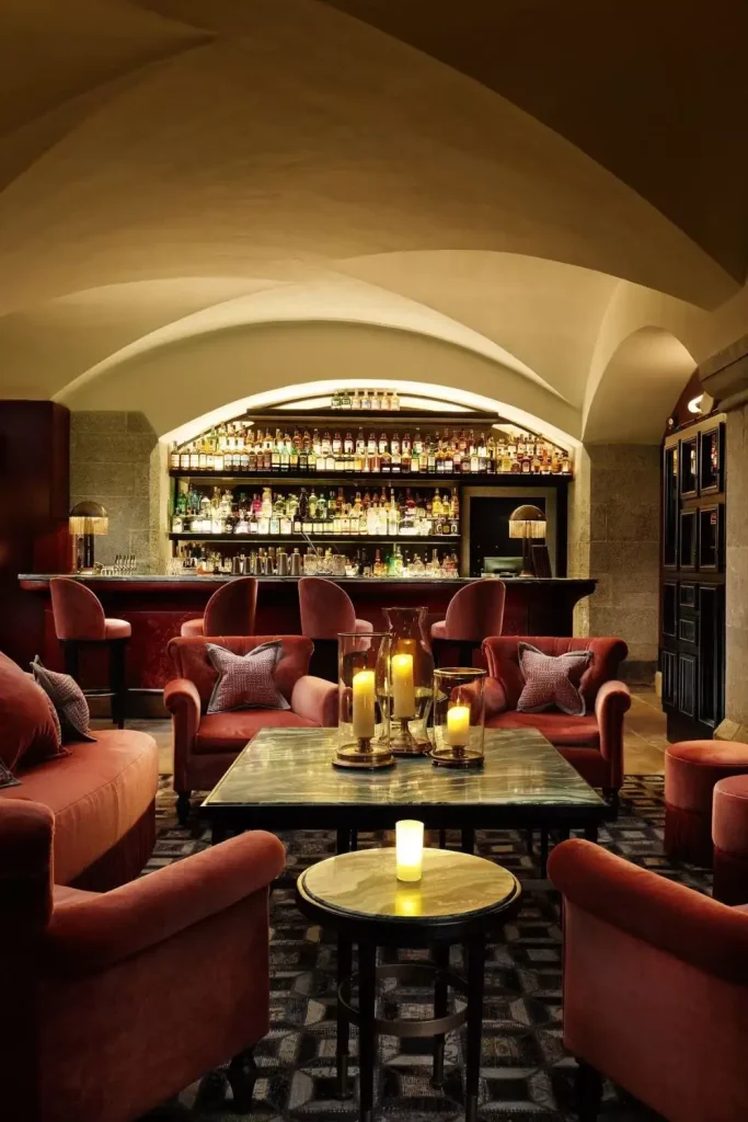 Irish castle wedding at Adare Manor, County Limerick — Tack Room cocktail bar interior featuring red lounge chairs with cushions, candlelit tables, and a fully stocked bar set against the historic castle setting.