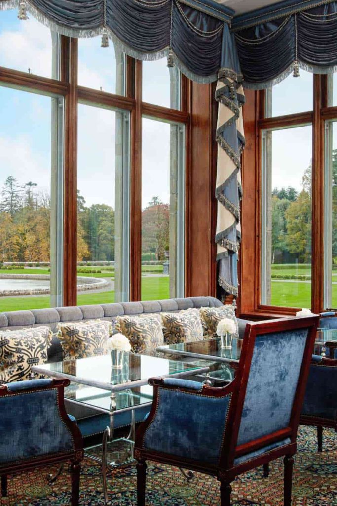 Irish castle wedding at Ashford Castle — Drawing Room with blue lounge seating, draped curtains, cushioned sofas, and estate views through tall windows.