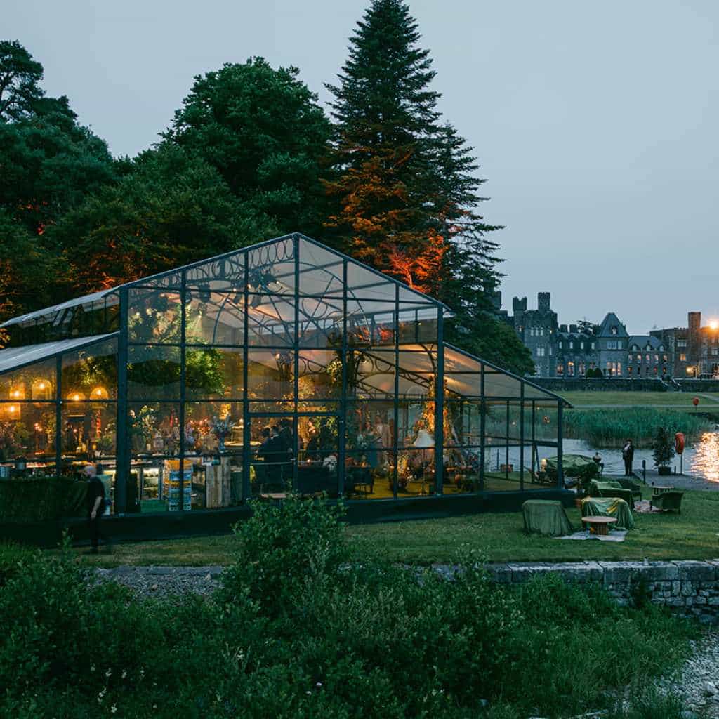 Irish castle wedding in Ireland — Orangerie at dusk glowing warm with guests celebrating inside during a lively wedding reception.