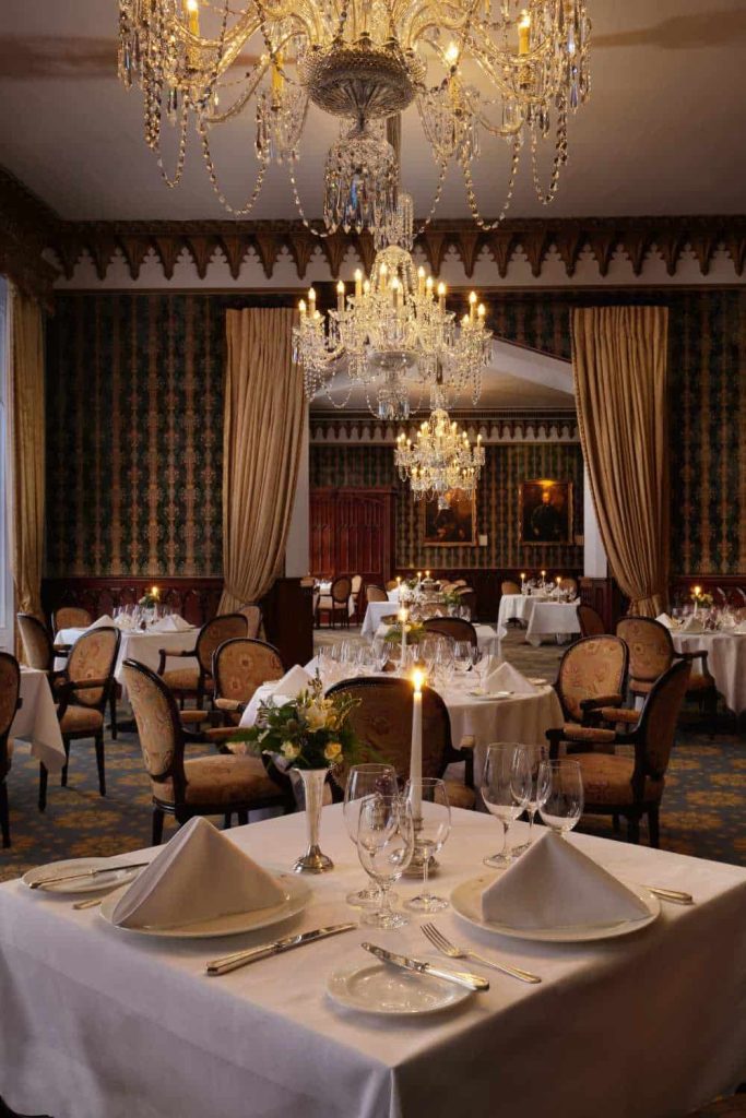Destination wedding at Dromoland Castle, County Clare — Earl of Thomond Restaurant prepared for dinner service with chandelier lighting, candlelit tables, and floral arrangements throughout the dining room.