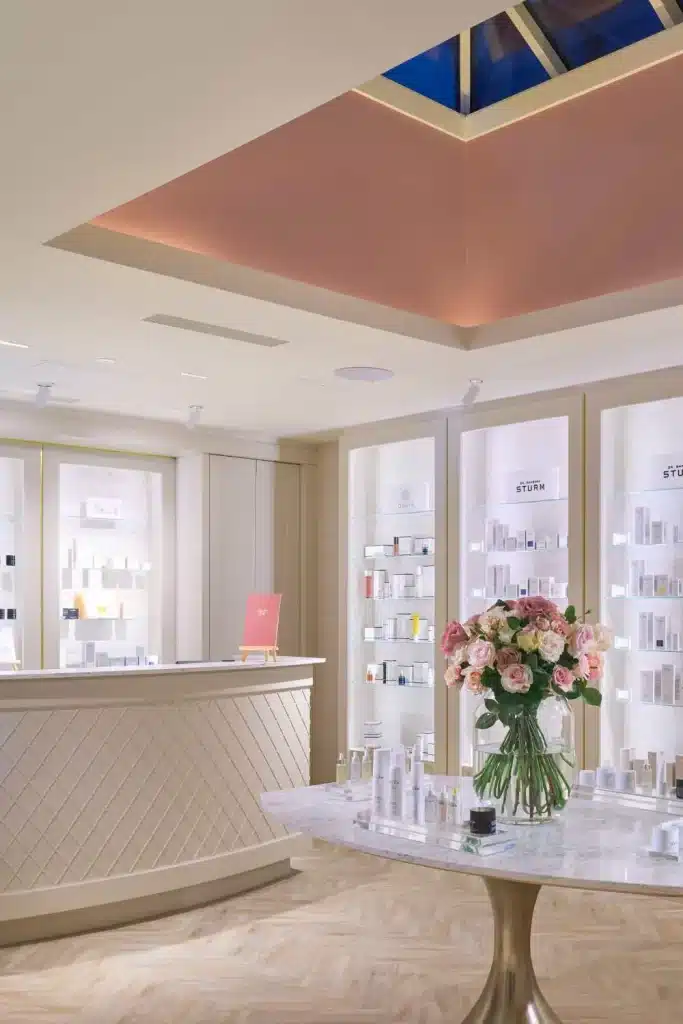 Upscale cosmetics shop interior with white display shelves, a marble table, and a vase of pink roses centerpiece.