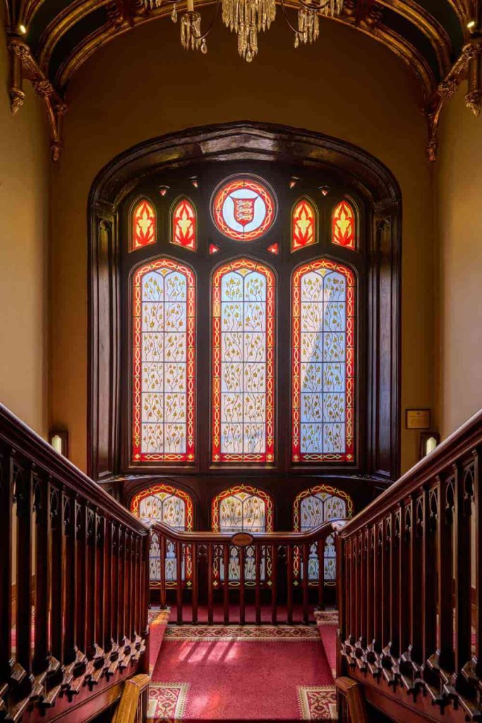 Destination wedding in Ireland at Dromoland Castle, County Clare — The Grand Staircase with carved wooden steps and a large stained-glass window featuring decorative patterned detailing.