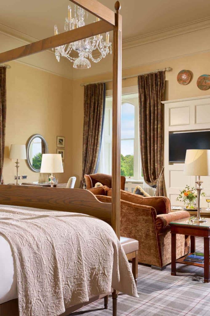 Destination wedding in Ireland at Dromoland Castle, County Clare — Viscount Stateroom with a wooden four-poster bed, separate lounge seating area, and television within the guest suite.