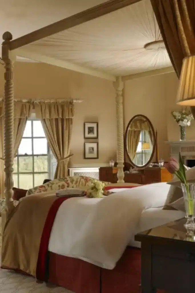 Destination wedding in Ireland at Mount Juliet Estate, County Kilkenny — Presidential Suite featuring a four-poster bed with plush bedding, a window with draped curtains, and a dresser with mirror within the manor house interior.