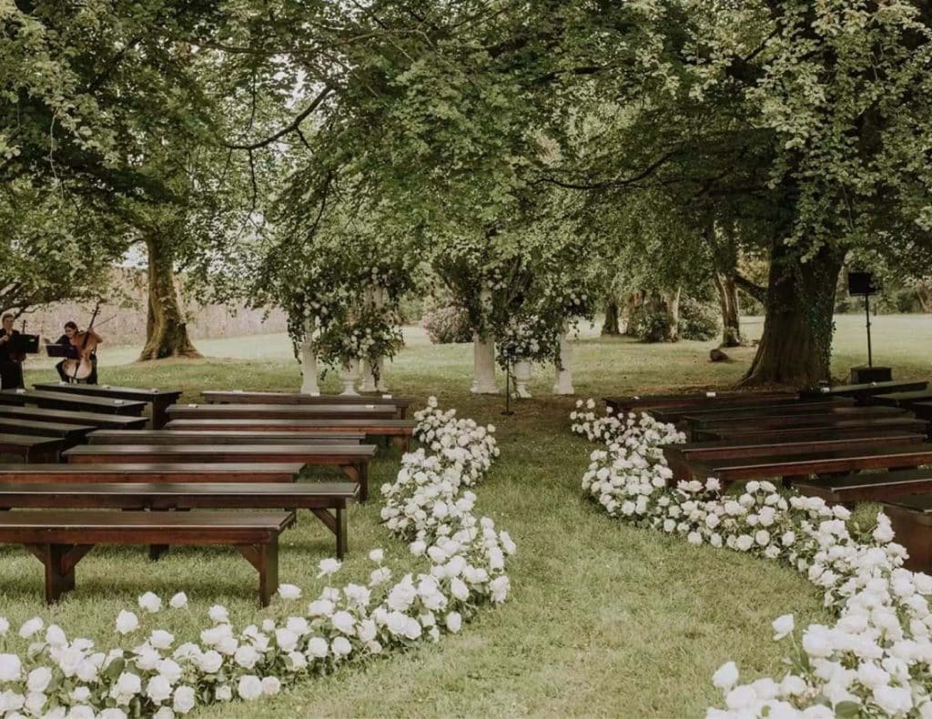 Destination wedding ceremony at Lough Eske Castle, County Donegal — rose-lined aisle through the forest during an outdoor celebration on the estate grounds.