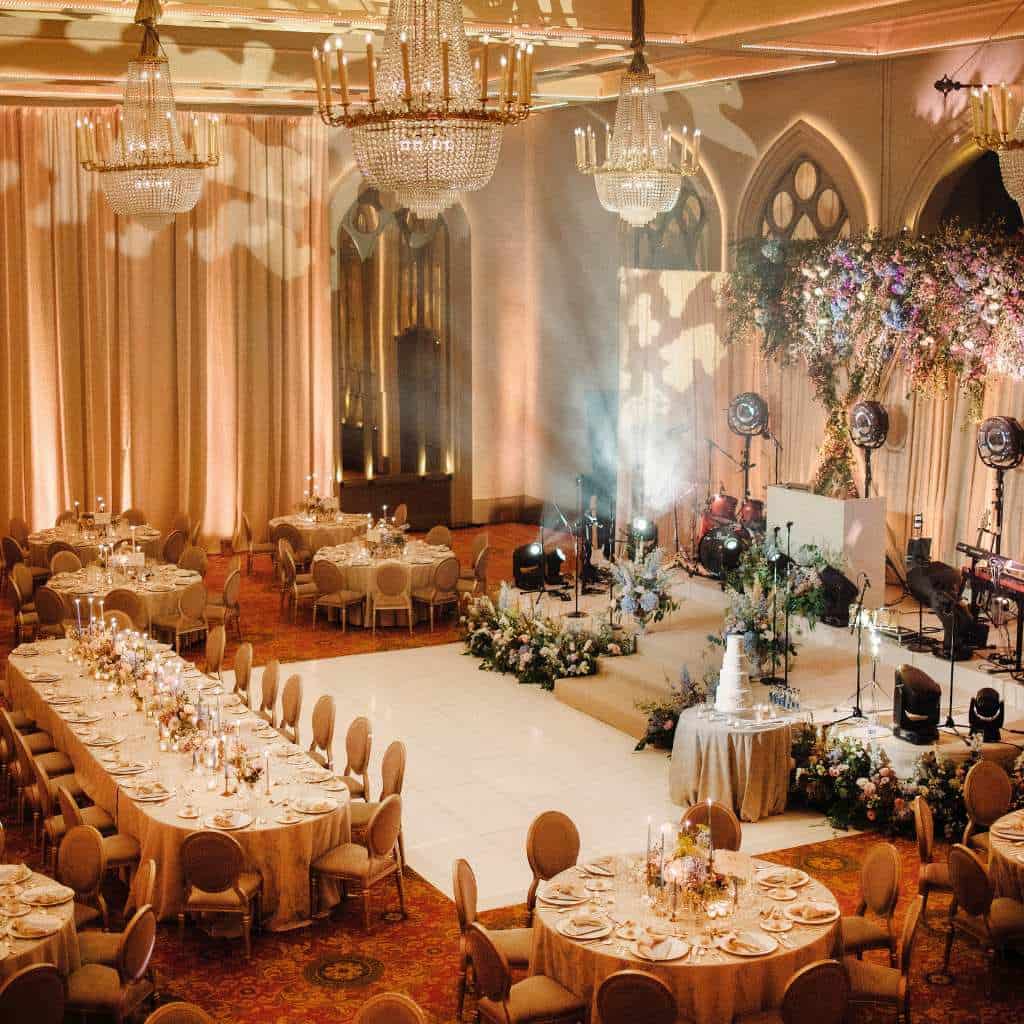 Irish castle wedding at Dromoland Castle, County Clare — ballroom set for a wedding dinner with dressed tables, a central dance floor, stage area, and chandeliers overhead.
