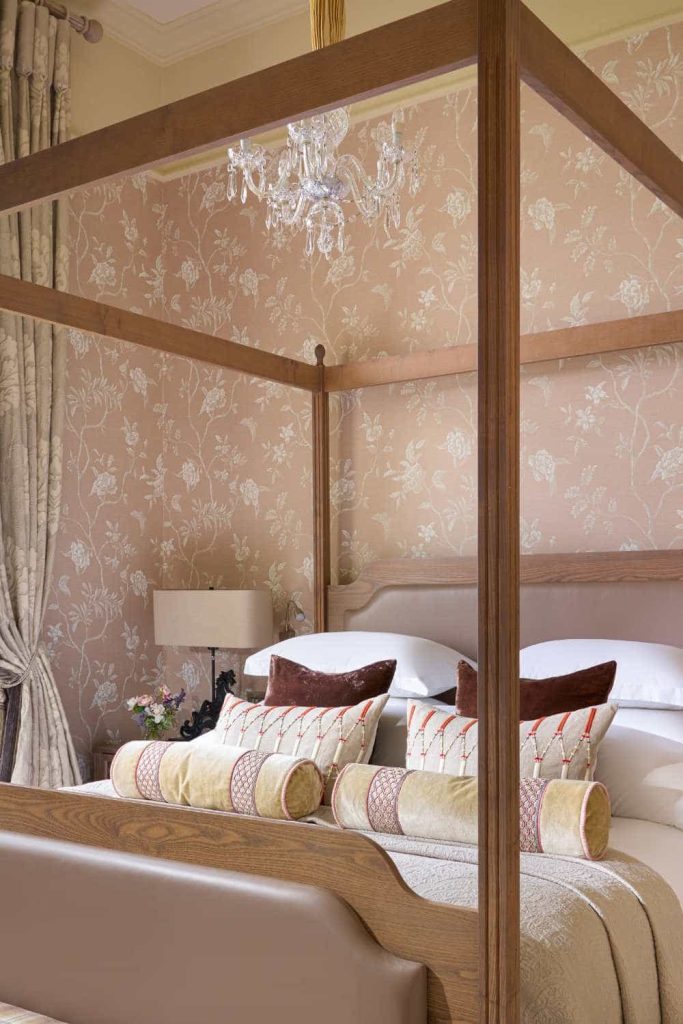 Irish destination wedding at Dromoland Castle, County Clare — Queen Anne Suite featuring a wooden four-poster bed, plush bedding with decorative cushions, and soft blush pink patterned wallpaper.