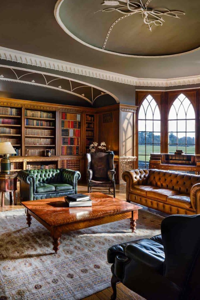 Wedding venue in Ireland at Luttrellstown Castle, County Dublin — library lounge with a large low coffee table, upholstered seating, book-lined shelving, and a window at the edge of the room.