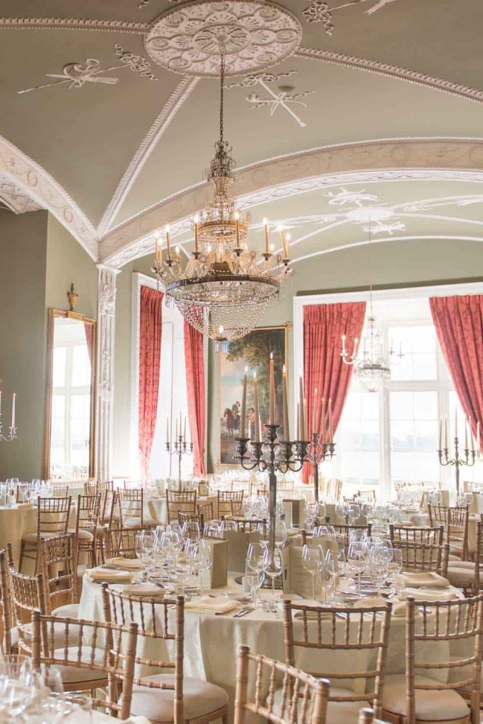Irish wedding venue at Luttrellstown Castle, County Dublin — The Van Stry Ballroom with a high-ceiling interior, ornate detailing, chandeliers, round dining tables, and tall candlelit centrepieces.