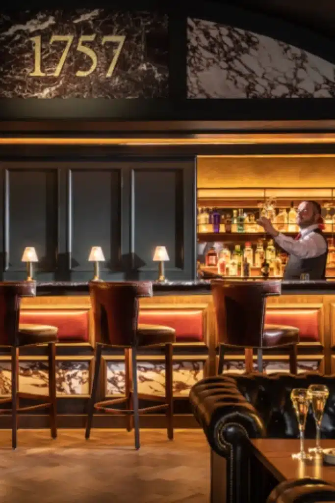 Destination wedding at Mount Juliet Estate, County Kilkenny, Ireland — The 1757 Bar with leather stools, softly lit table lamps along the bar, and a bartender serving behind the counter.