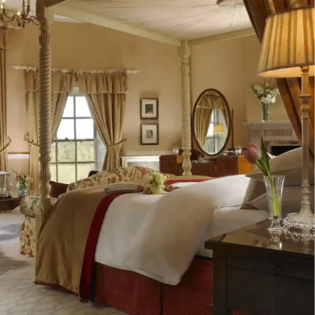 Destination wedding accommodation at Mount Juliet Estate, County Kilkenny, Ireland — bedroom with a four-poster bed, plush bedding, draped curtains, and a bedside locker topped with a floral arrangement.