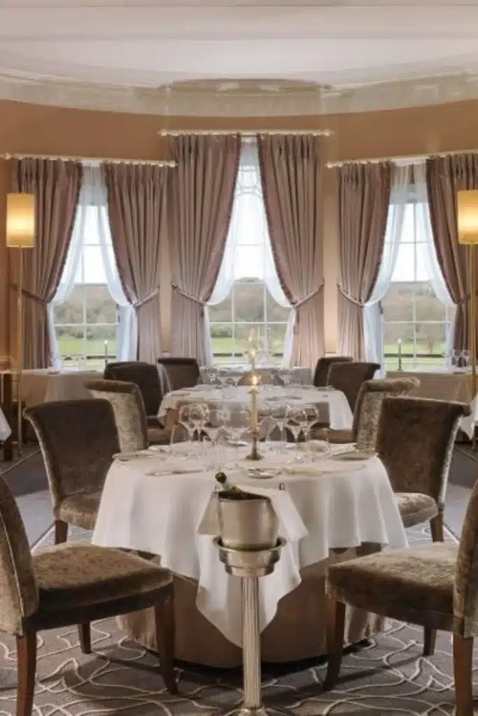 Destination wedding in Ireland at Mount Juliet Estate, County Kilkenny, Ireland — dining table set within the Lady Helen Restaurant featuring round banquet seating, a wine cooler with bottle, and curtained windows in the background.