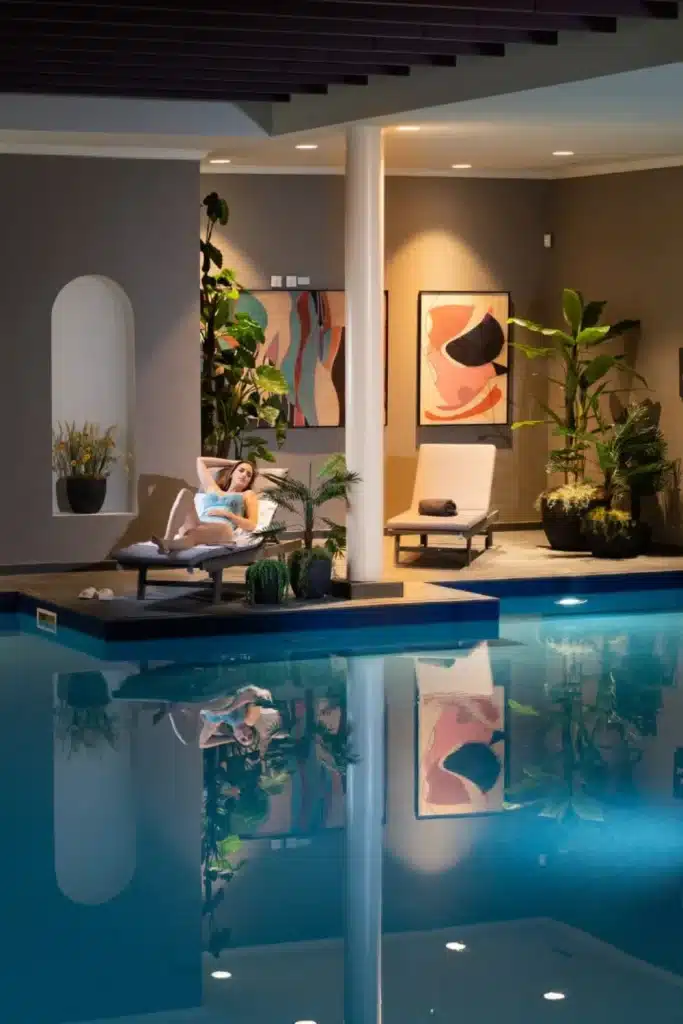 Destination wedding at Mount Juliet Estate, County Kilkenny, Ireland — indoor pool area with two lounge chairs at the water’s edge, one occupied by a guest, alongside abstract wall artwork and greenery.