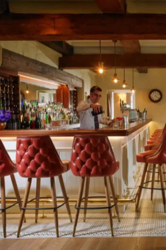 Wedding venue at Mount Juliet Estate, County Kilkenny, Ireland — The Saddle Bar featuring red high stools and a bartender pouring a drink behind the bar.