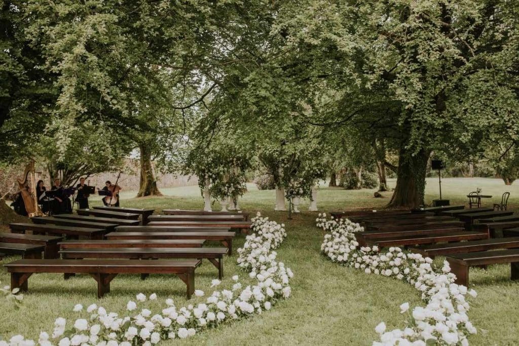 Bespoke Bride feature on choosing a wedding date that balances budget and guest experience, illustrated by a woodland wedding ceremony with a rose-lined aisle at Lough Eske Castle.